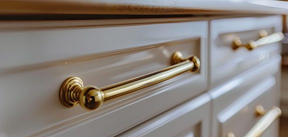 Golden furniture handle, on white wooden kitchen cabinet . Small depth of field. used as background. toned. with copy space image. Place for adding text or design